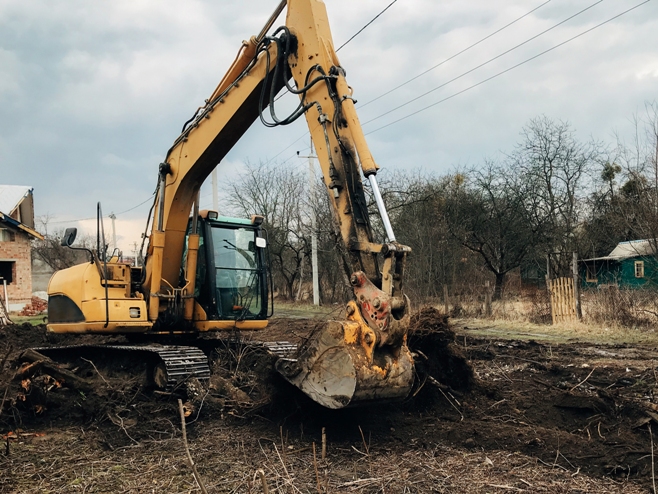 Excavator uprooting trees on land in countryside